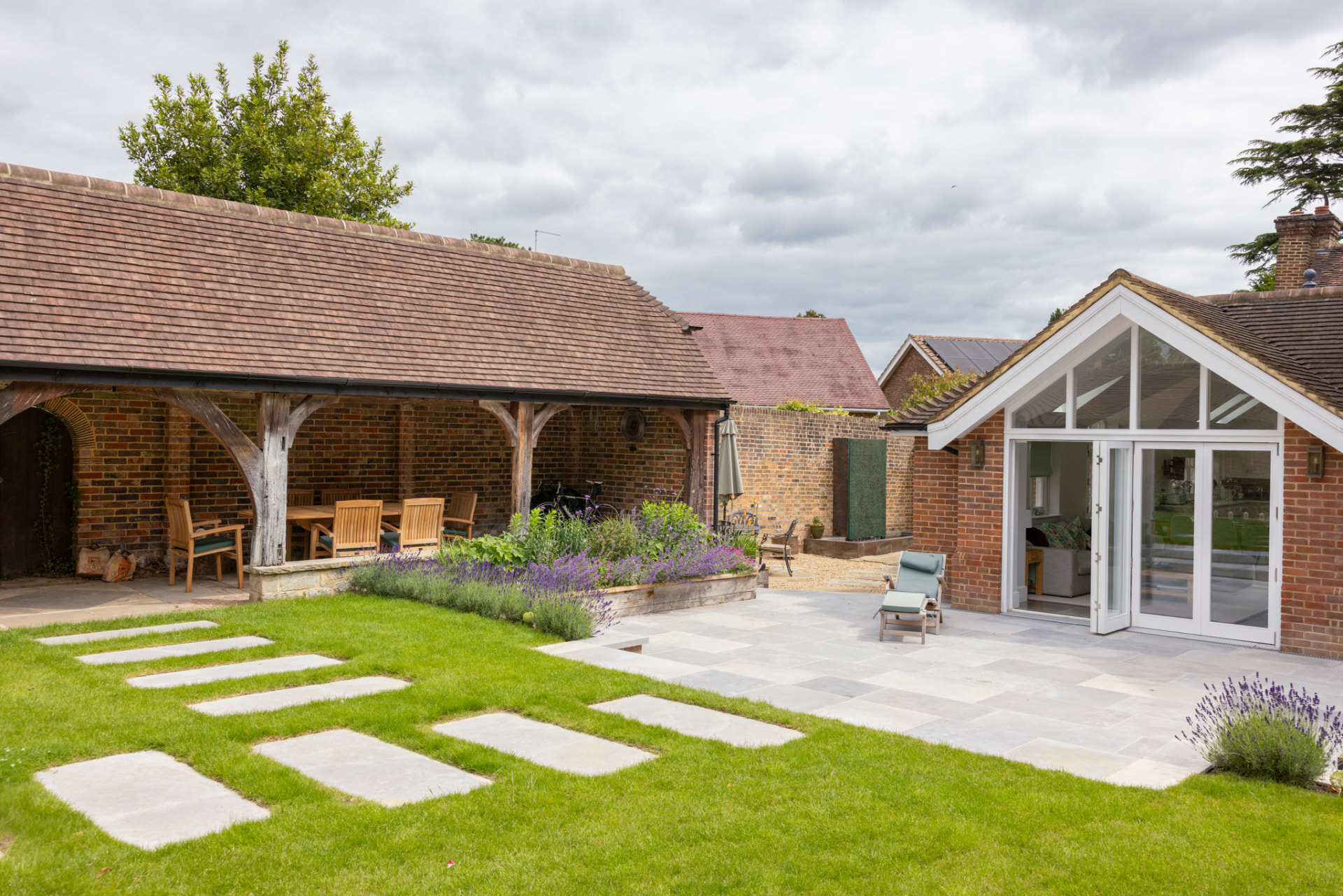 The finished country courtyard garden built from that design, with the oak pergola, brick buildings, stepping stones across the lawn, stone patio and established lavender planting