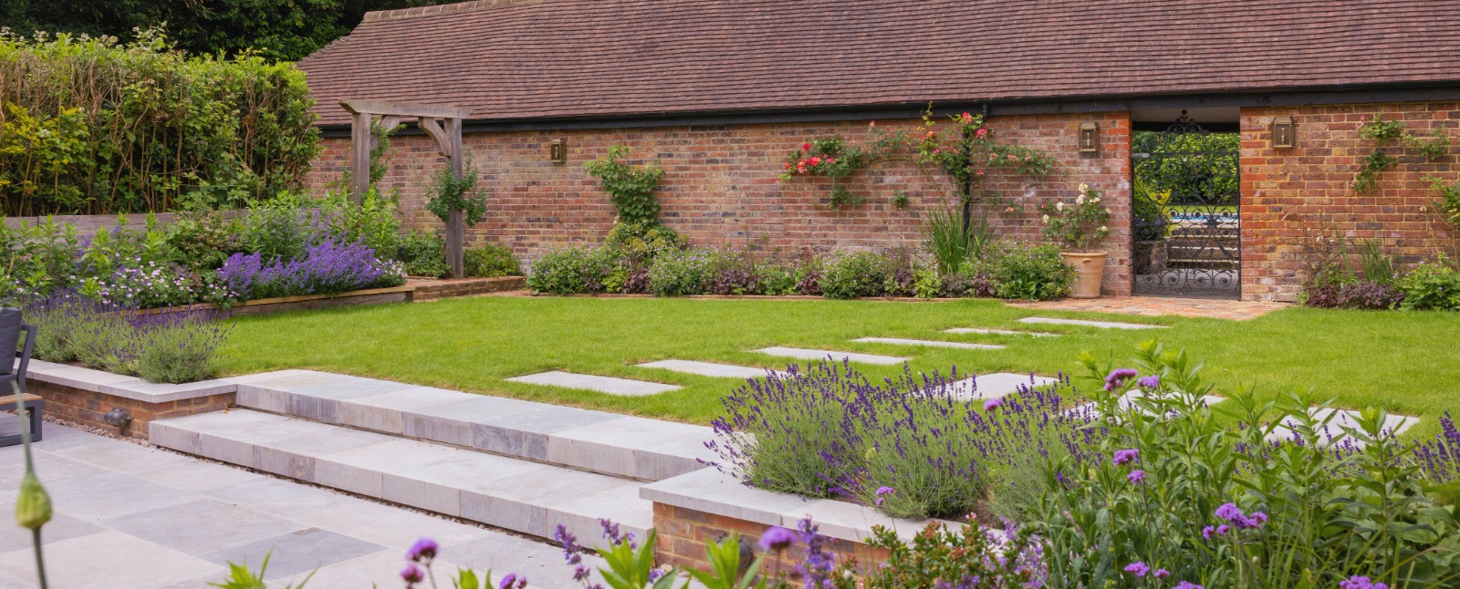 A finished country garden with stone terraces, lavender borders and a brick barn