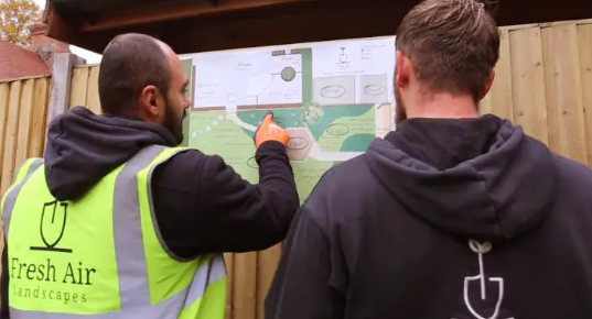 Alistair Gardner and a colleague in Fresh Air Landscapes clothing reviewing a garden design plan against a fence