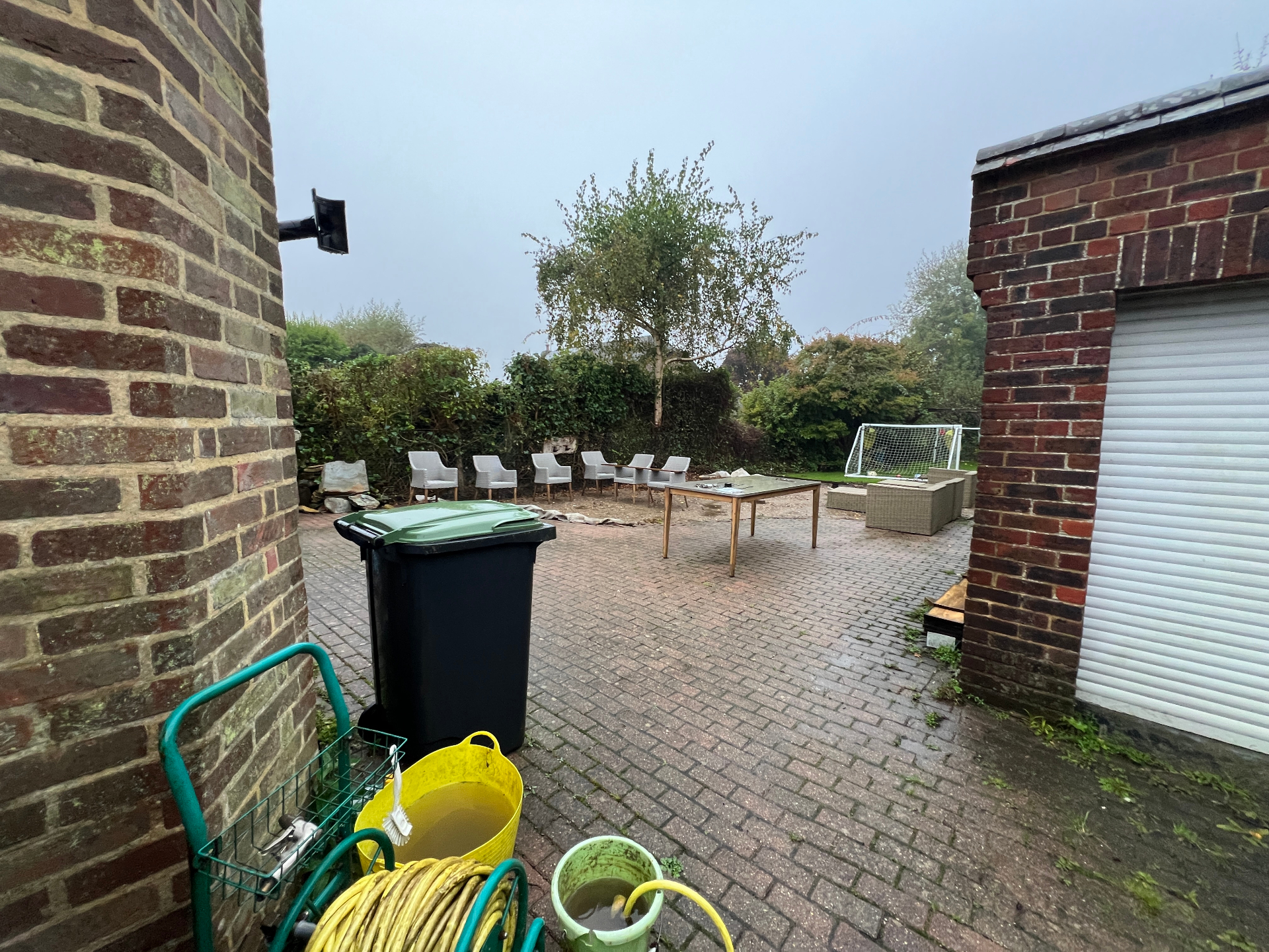 Original family garden - worn block paving with mismatched furniture against brick walls