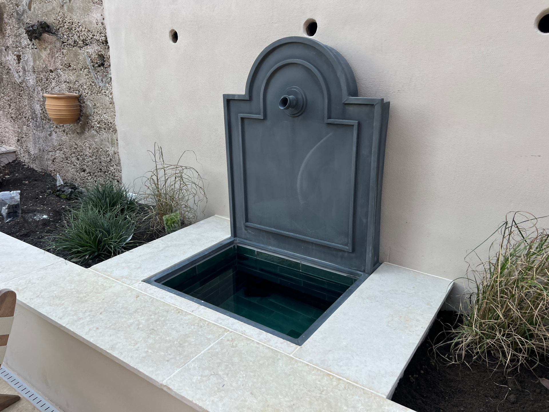 Medi Garden - lead fountain against the lime-rendered wall with grasses and terracotta pot