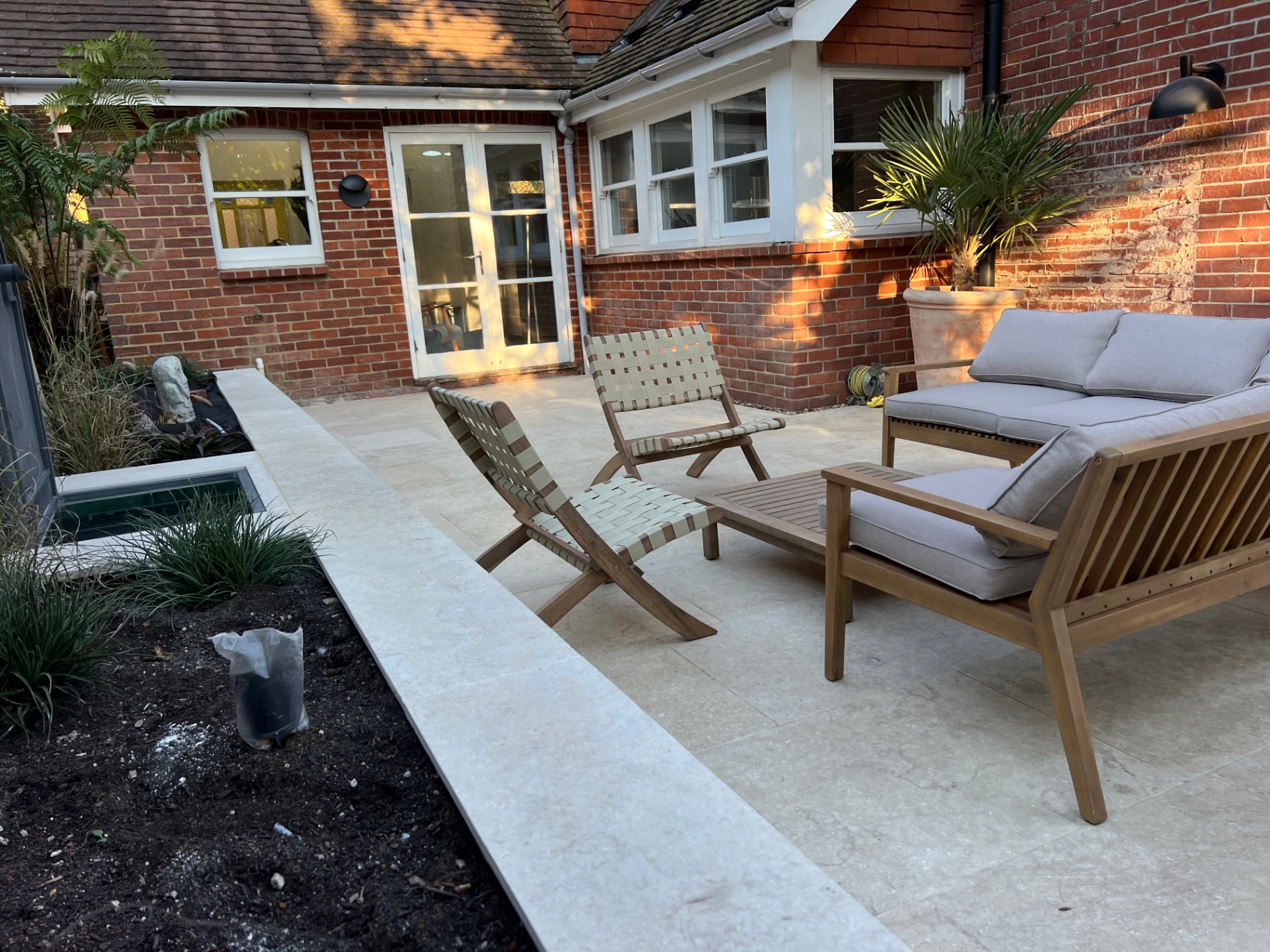 Medi Garden - wider view of the travertine courtyard with woven lounge chairs and planted edges