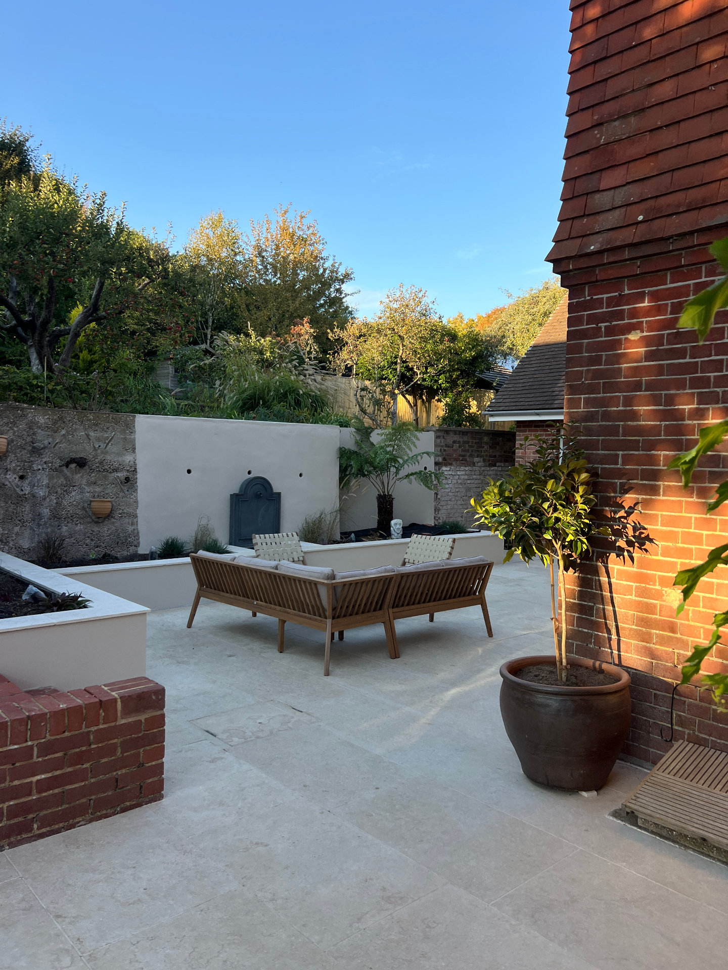 Medi Garden - travertine terrace at golden hour with lead fountain wall and bay tree in terracotta pot