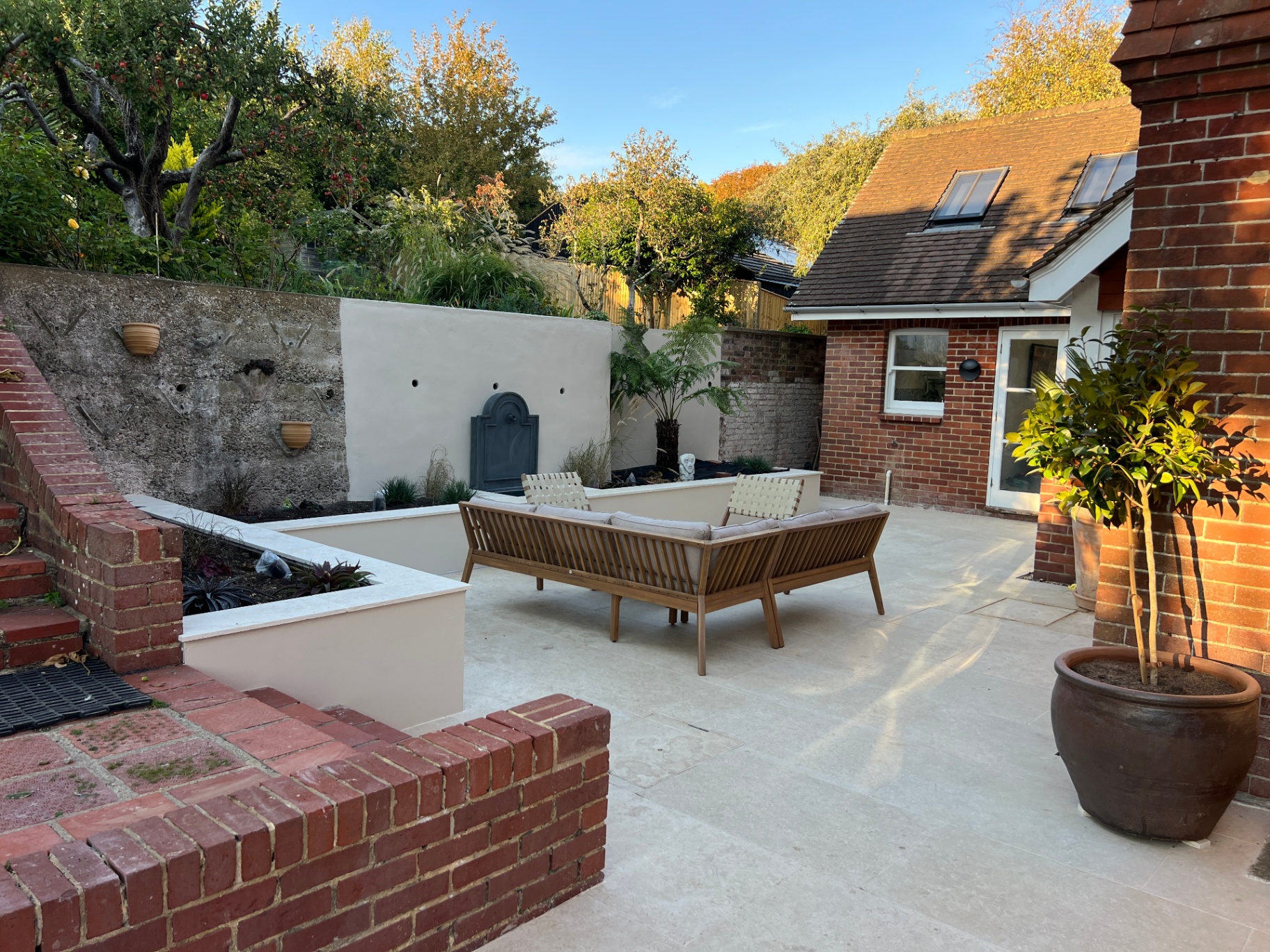 Medi Garden - full courtyard view with rendered wall, raised beds and timber sofa on travertine paving