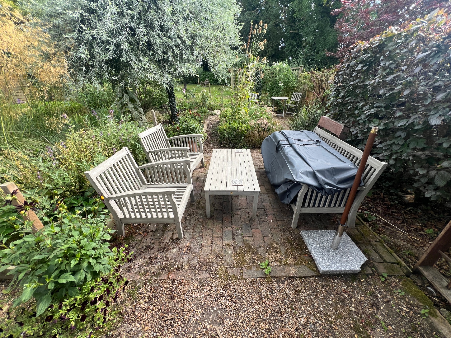 Original garden - weathered teak seating on a small brick patio surrounded by overgrown borders